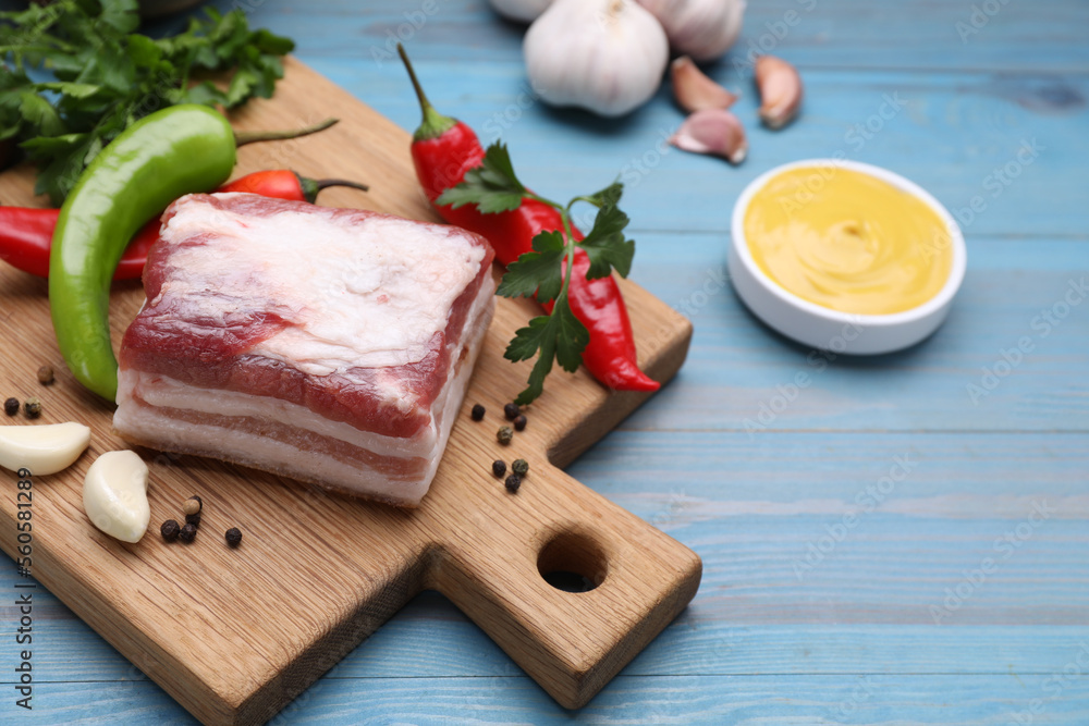 Piece of pork fatback with garlic and chilli pepper on light blue wooden table Piece of pork fatback with garlic and chilli pepper on light blue wooden table