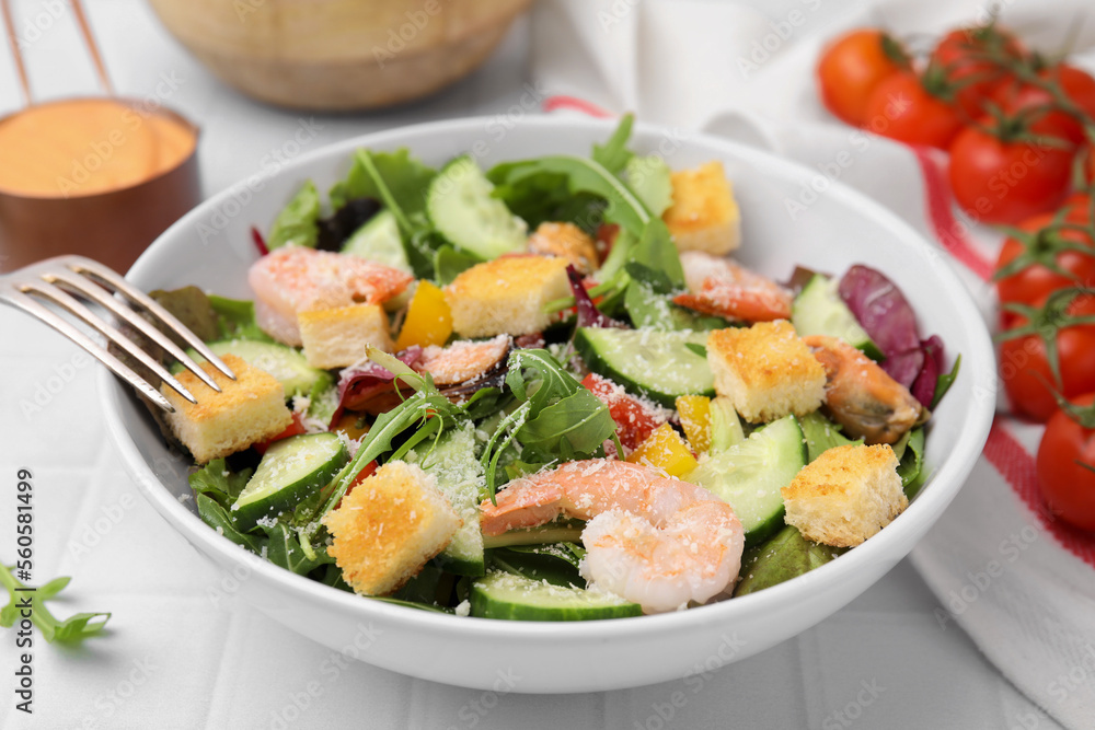 Delicious salad with croutons, cucumber and shrimp served on white tiled table, closeup Delicious salad with croutons, cucumber and shrimp served on white tiled table, closeup