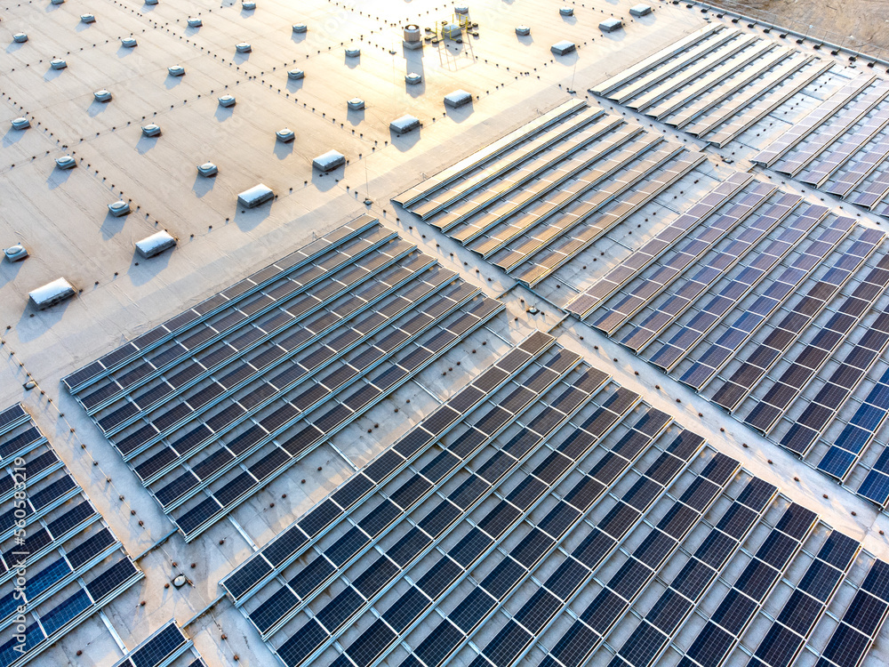 Obraz premium Large solar panel array farm on a commercial warehouse building in sunset aerial view