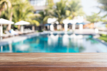 Empty wood table top and blurred swimming pool in tropical resort in summer banner background - can used for display or montage your products.