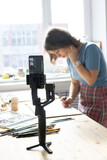 Young woman painting a picture with watercolor and filming video at wooden table