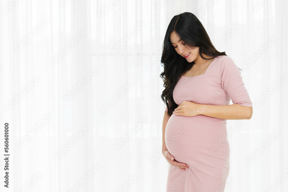 happy pregnant woman stroking belly on window background - obrazy, fototapety, plakaty 