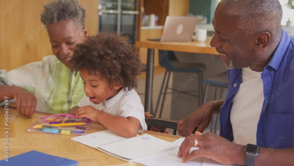 Multi-generation family with grandparents helping grandson with homework at home sitting around table - shot in slow motion Multi-generation family with grandparents helping grandson with homework at home sitting around table - shot in slow motion