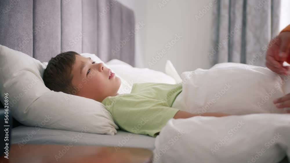Mother caring for sick mixed race boy lying in bed with flu and cough, measuring temperature using hand. Little preschool boy at home with fever. African american mom giving health care slow motion Mother caring for sick mixed race boy lying in bed with flu and cough, measuring temperature using hand. Little preschool boy at home with fever. African american mom giving health care slow motion