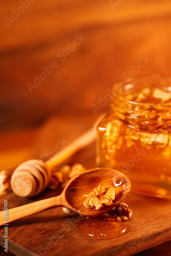 Honey mixed with nuts flowing from a wooden spoon in a honey jar. Wood texture background. Close up photo of a healthy breakfast. Vertical image.