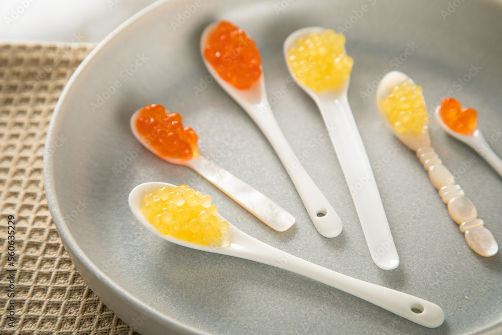 Kaviar von orange Keta Lachs und gelb Saibling mit Auswahl von Löffel aus Perlmutt, Plastik, Porzellan auf hell Steingut Teller und Marmor Hintergrund Kaviar von orange Keta Lachs und gelb Saibling mit Auswahl von Löffel aus Perlmutt, Plastik, Porzellan auf hell Steingut Teller und Marmor Hintergrund