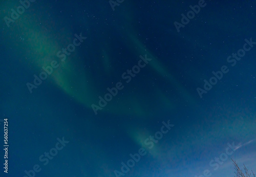 Green and purple northern lights in iceland with the sky bluish by the moon