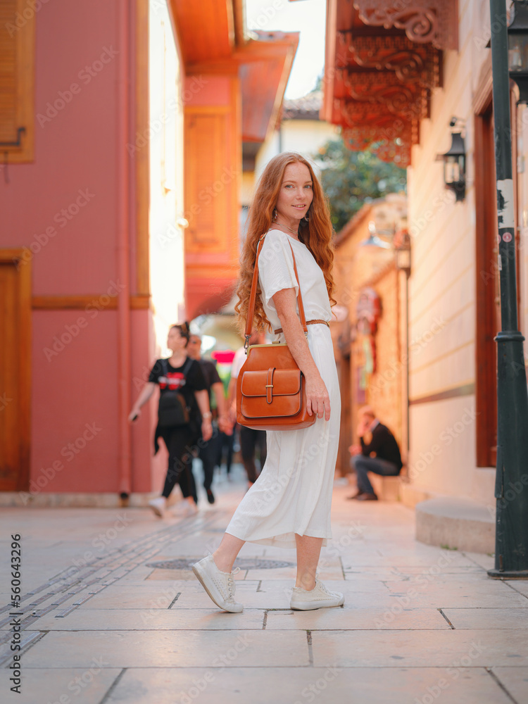Obraz premium Happy woman tourist on background of blooming street of Antalya. female tourist traveler discover interesting places and popular attractions and walks in the old city Kalechi of Antalya, Turkey.