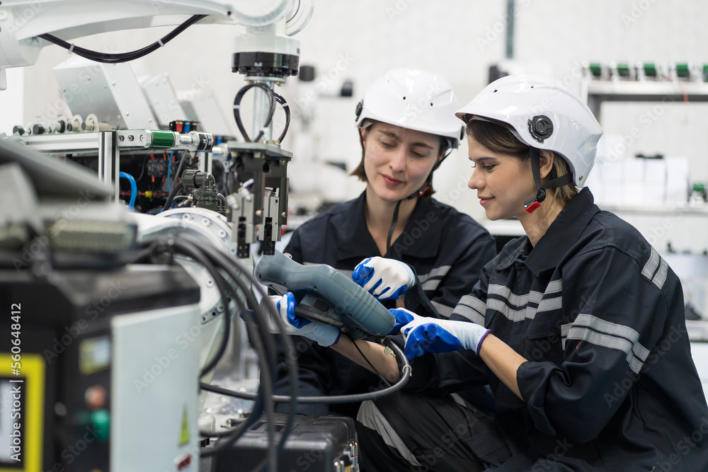 Two female engineers control autonomous mobile robot or AMR in the manufacturing automation and robotics academy room. Group of female engineers training or maintenance AI robot Two female engineers control autonomous mobile robot or AMR in the manufacturing automation and robotics academy room. Group of female engineers training or maintenance AI robot