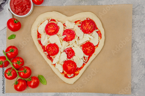 Pizza Margherita shaped heart with cherry tomatoes, mozzarella and basil on a gray concrete background. Food concept for Valentine's Day. Copy space.