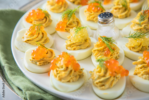 Gefüllte teuflische russische Eier mit Dill und orange Keta Lachs und gelb Saibling Kaviar auf Eierteller, Serviette grün, Silber Teller und Marmor Hintergrund hell