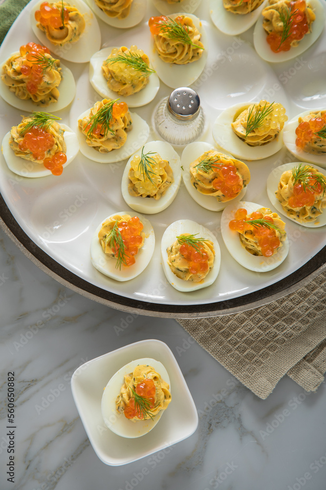 Gefüllte teuflische russische Eier mit Dill und orange Keta Lachs und gelb Saibling Kaviar auf Eierteller, Serviette grün, Silber Teller und Marmor Hintergrund hell Gefüllte teuflische russische Eier mit Dill und orange Keta Lachs und gelb Saibling Kaviar auf Eierteller, Serviette grün, Silber Teller und Marmor Hintergrund hell