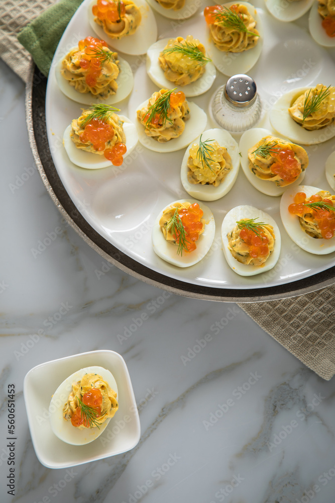 Gefüllte teuflische russische Eier mit Dill und orange Keta Lachs und gelb Saibling Kaviar auf Eierteller, Serviette grün, Silber Teller und Marmor Hintergrund hell Gefüllte teuflische russische Eier mit Dill und orange Keta Lachs und gelb Saibling Kaviar auf Eierteller, Serviette grün, Silber Teller und Marmor Hintergrund hell