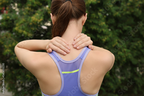 Young woman suffering from neck pain outdoors, back view