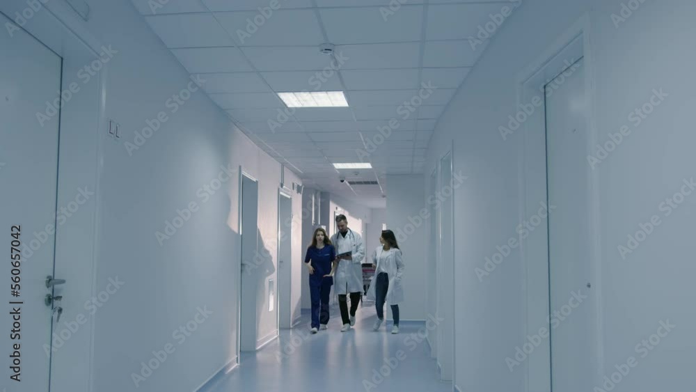 Three doctors are walking down the corridor of the hospital looking at a tablet and discussing the treatment of patients Three doctors are walking down the corridor of the hospital looking at a tablet and discussing the treatment of patients