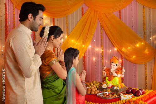 Indian nuclear family in traditional dress celebrating Ganesh chaturthi. The family is worshiping Lord Ganesh on Ganesh Chaturthi by folding their hands and eyes closed - Prayer photo