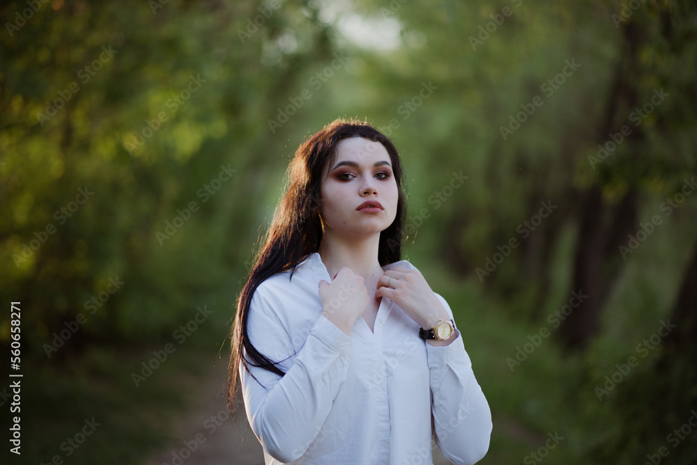 Sexy sensual brunette walks in a summer forest at sunset in a white blouse and jeans Sexy sensual brunette walks in a summer forest at sunset in a white blouse and jeans