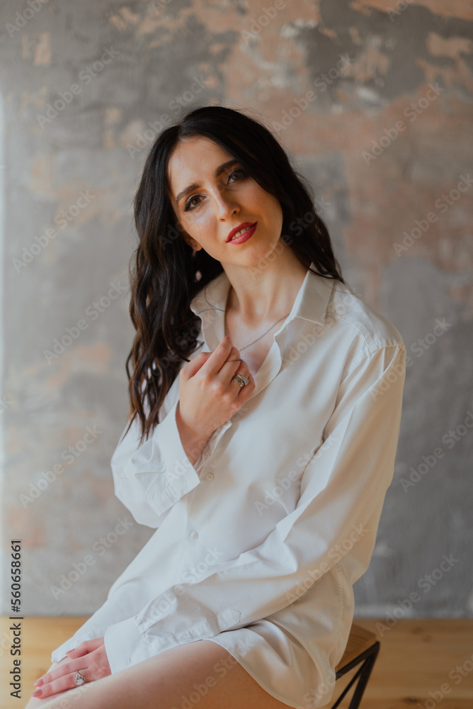 Fototapeta premium Sexy young brunette girl in a white shirt and lingerie in a loft photo studio