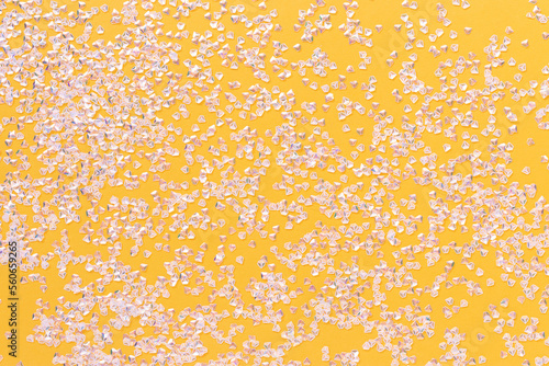 Small silver crystal confetti on a bright yellow background. Glittering texture.