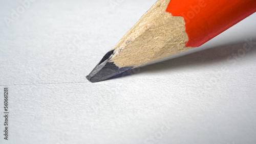 Wooden red graphite pencil draws a line on a white paper