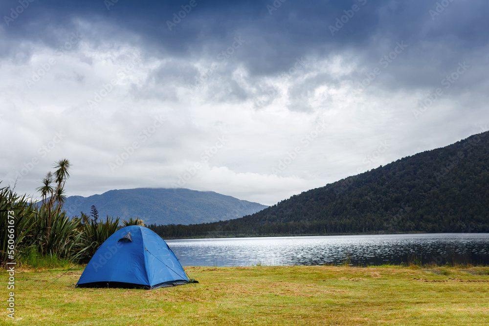 Camping and tent under the rainy forest near the lake with beautiful mountains background