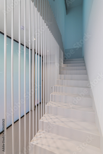 Beautiful white staircase to the second floor with soft blue lighting. Original design solution of the floor-to-ceiling fence made of metal white rods gives the effect of weightlessness. © Pavel