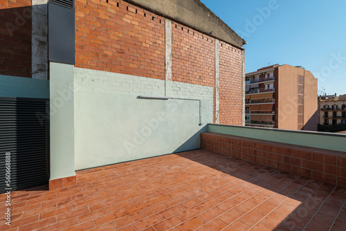 An empty spacious terrace on the second floor of a large house with a brick red floor for relaxing on warm summer evenings in the sun of the passing day. Sunlight illuminates the site. photo