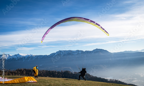 Men on a grassy slope prepare the glider for paragliding from Vetriolo Terme, Trento province - Trentino Alto Adige - Paragliding school - Italy