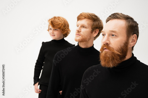adult bearded men and redhead boy in black turtlenecks looking away isolated on grey.