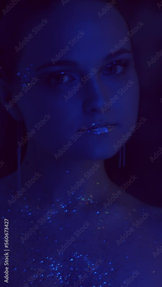 Vertical video. Glitter makeup. Neon girl. Nightclub fashion. Blue purple color flash light woman face with sparkling metallic eyeshadow lips in mirror on dark. Vertical video. Glitter makeup. Neon girl. Nightclub fashion. Blue purple color flash light woman face with sparkling metallic eyeshadow lips in mirror on dark.