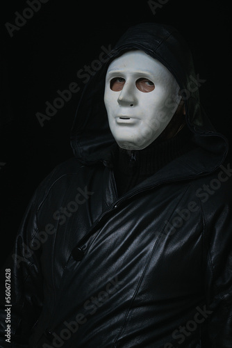 Man in terrible face mask staring at camera against dark background cloak with hood