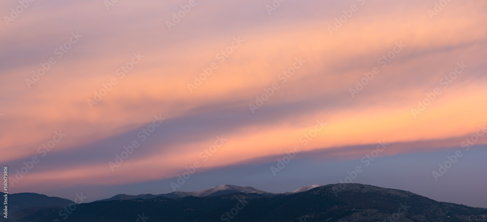 Stunning sunset with beautiful shades of orange, pink, purple and blue colors with the silhouette of a mountain range. Wallpaper, natural background with copy space.