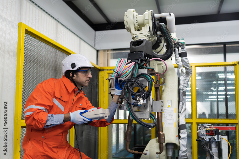Male engineer repair or maintenance automatic robot arm system in the manufacturing automation and robotics academy room. Male technician working with robotic arm system. Robot maintenance concept Male engineer repair or maintenance automatic robot arm system in the manufacturing automation and robotics academy room. Male technician working with robotic arm system. Robot maintenance concept