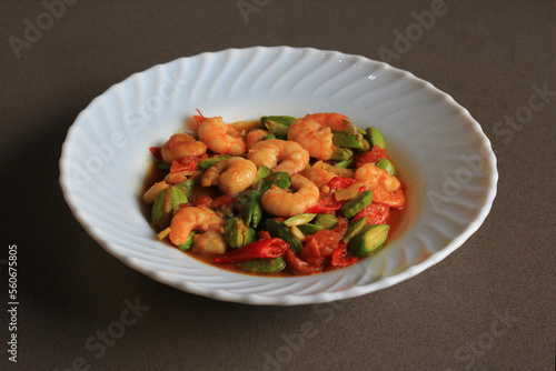 Chili prawns or Sambal Udang with petai or pete or mlanding (Parkia speciosa) cooked with mashed red chili and tomato in white plate, on black background. Indonesia cuisine food.