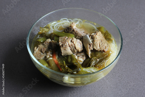 sup bakut or baikut babi sayur asin, is popular Chinese Indonesian pork rib soup with pickled cabbage or mustard greens and vermicelli in clear bowl, on black background, front view. photo