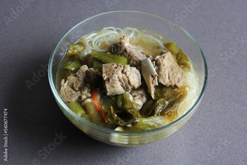 sup bakut or baikut babi sayur asin, is popular Chinese Indonesian pork rib soup with pickled cabbage or mustard greens and vermicelli in clear bowl, on black background. photo