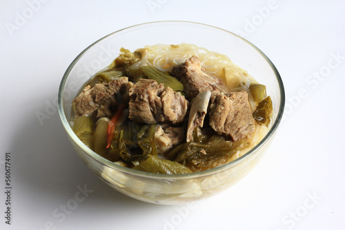 sup bakut or baikut babi sayur asin, is popular Chinese Indonesian pork rib soup with pickled cabbage or mustard greens and vermicelli in clear bowl, isolated on white background, front view.