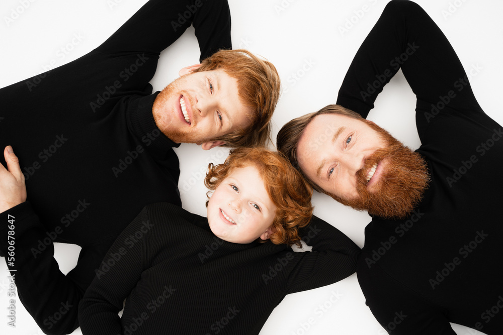 top view of smiling redhead boy with bearded grandfather and dad in black turtlenecks lying on white background. top view of smiling redhead boy with bearded grandfather and dad in black turtlenecks lying on white background.