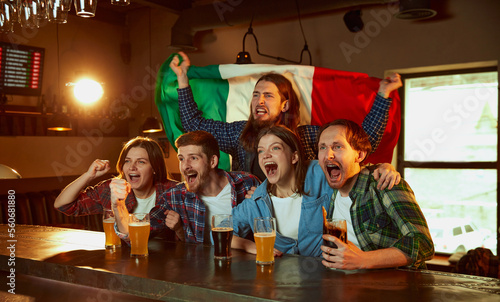 Group of young people, men and women watching match at pub. Fans emotionally cheering up favourite sport team. Italy