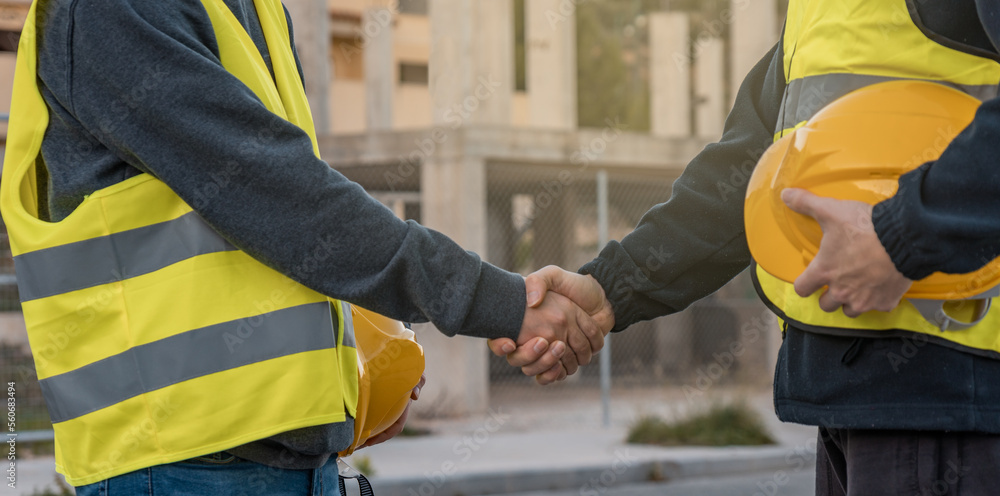 Dos operarios de construcción, estrechándose la mano y de fondo un edificio en obra. Dos operarios de construcción, estrechándose la mano y de fondo un edificio en obra.