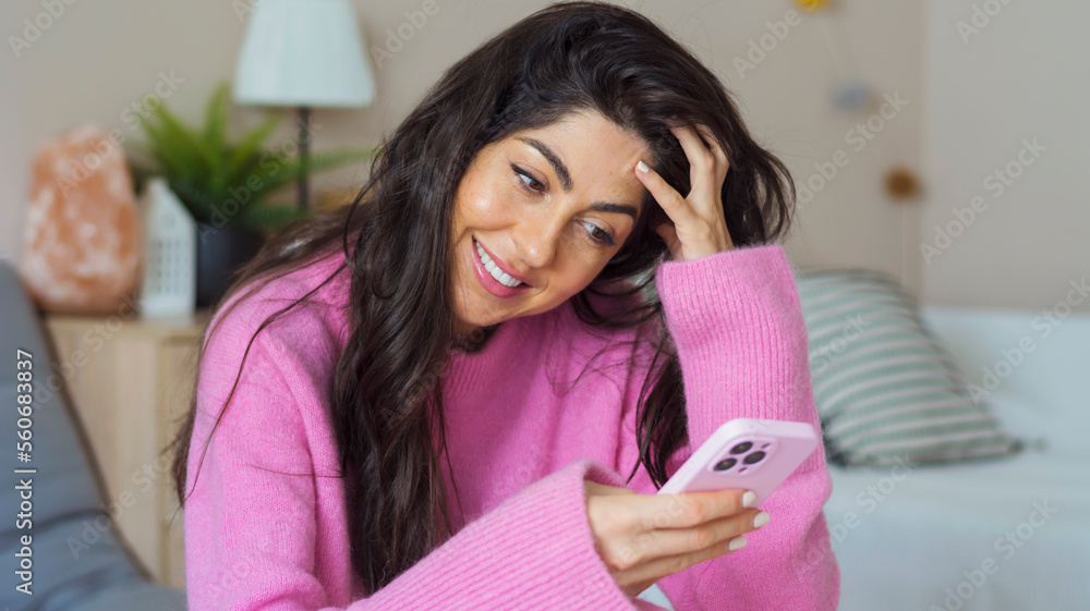Beautiful  young happy woman with pink sweater  sitting at home and  using mobile phone