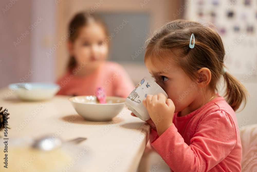 Two sisters have dinner together in the kitchen, baby girl drinks from a cup. Two sisters have dinner together in the kitchen, baby girl drinks from a cup.