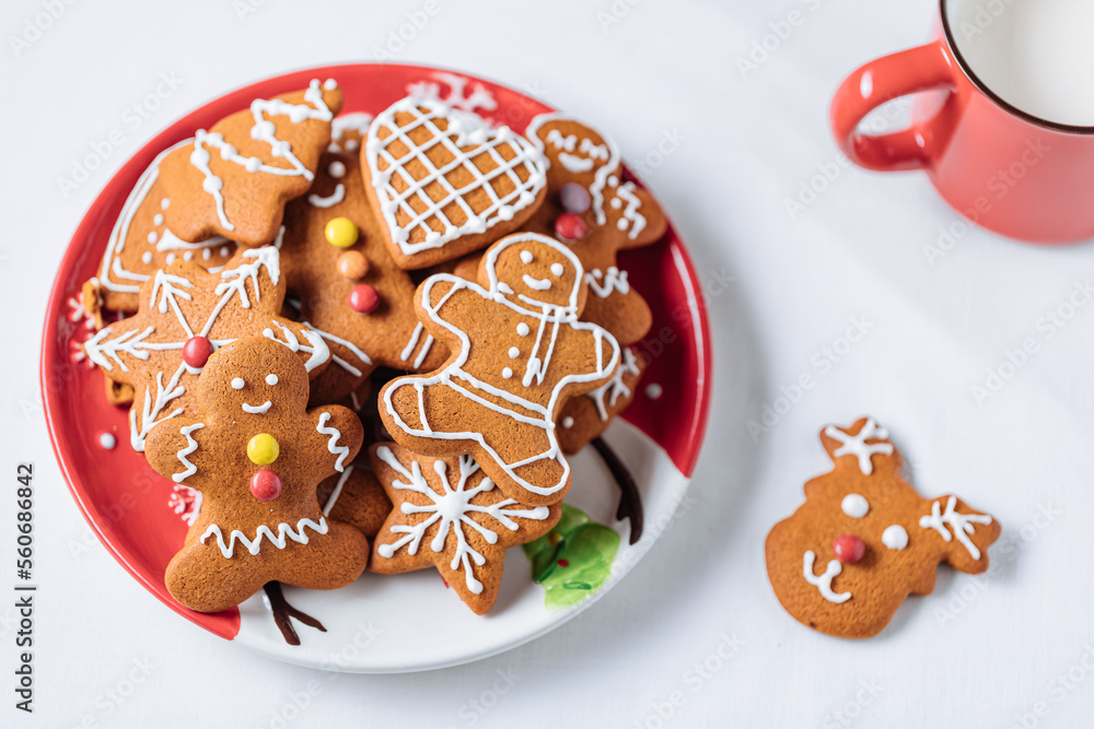 Gingerbread cookies in shape of ginger man placed on red plate. White background. Traditional Christmas dessert decorated. Playful and happy.