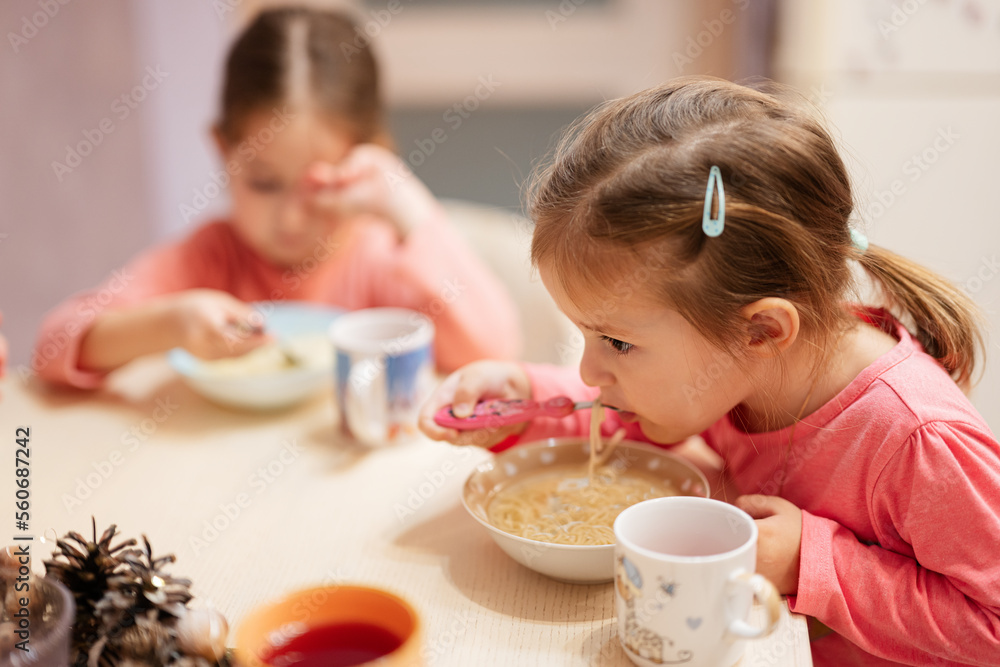 Two sisters have dinner together in the kitchen, baby girl eats bouillon. Two sisters have dinner together in the kitchen, baby girl eats bouillon.