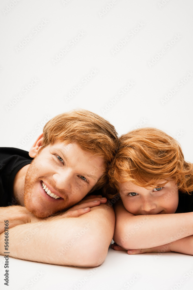 young and cheerful man with red haired son lying with crossed arms and looking at camera on light grey background. young and cheerful man with red haired son lying with crossed arms and looking at camera on light grey background.