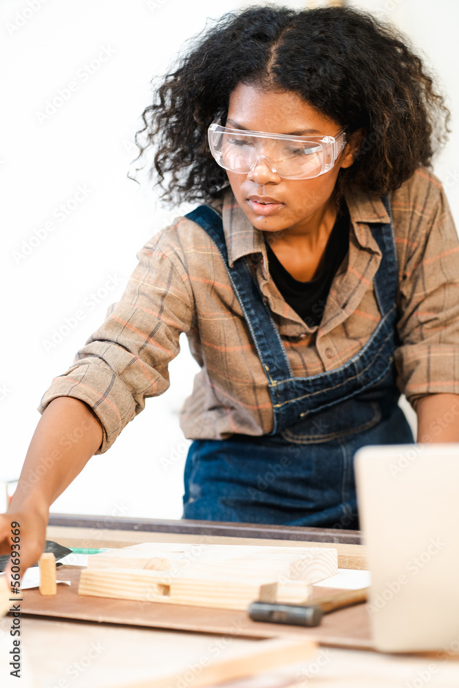 Young female carpenter is working in woodwork DIY furniture in carpentry workshop. Multiracial woman woodworker busy working with lumber plank designing at workbench. Skill craftsman woodworking. Young female carpenter is working in woodwork DIY furniture in carpentry workshop. Multiracial woman woodworker busy working with lumber plank designing at workbench. Skill craftsman woodworking.