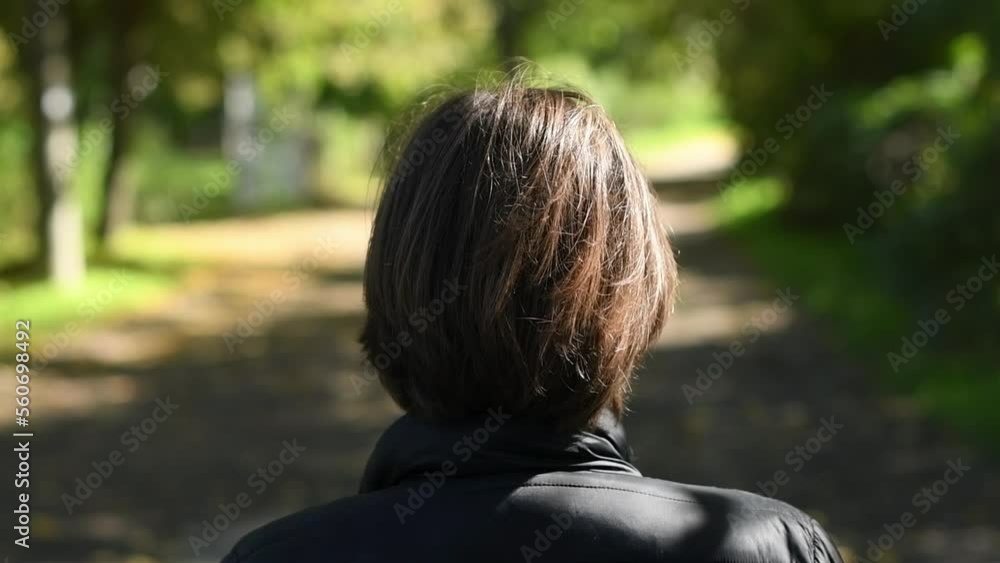 Rear view of female person standing alone in public park and looking along the road in front of her Rear view of female person standing alone in public park and looking along the road in front of her