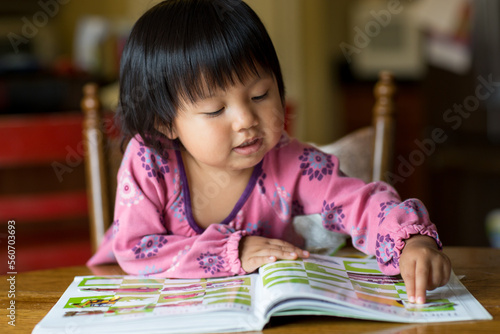 Girl patting down a sticker book at a dining room table photo