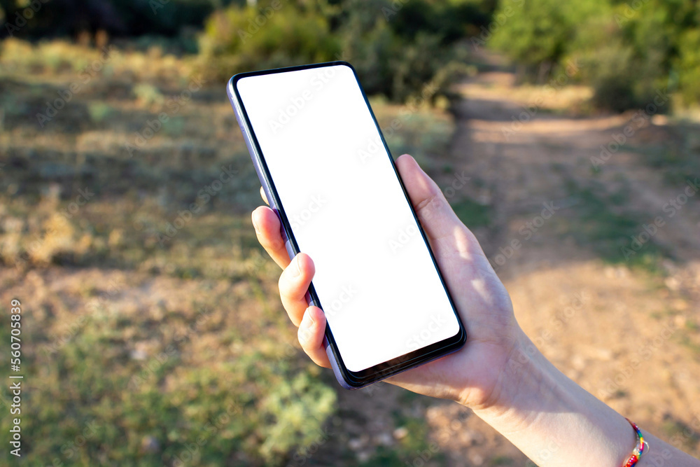 Hand holding phone with blank white screen while walking in the nature ...