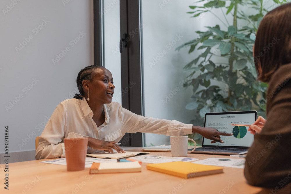 Glad black woman discussing graph with colleague Glad black woman discussing graph with colleague